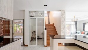 Una cocina moderna con encimera de mármol, una escalera de madera y un ventanal que da a un comedor.