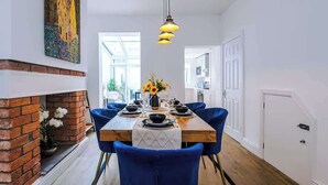A dining area with a brick fireplace, a wooden table set for six, and blue chairs. - Stylish 3-Bed City Centre Home, Private Parking! (Chester)