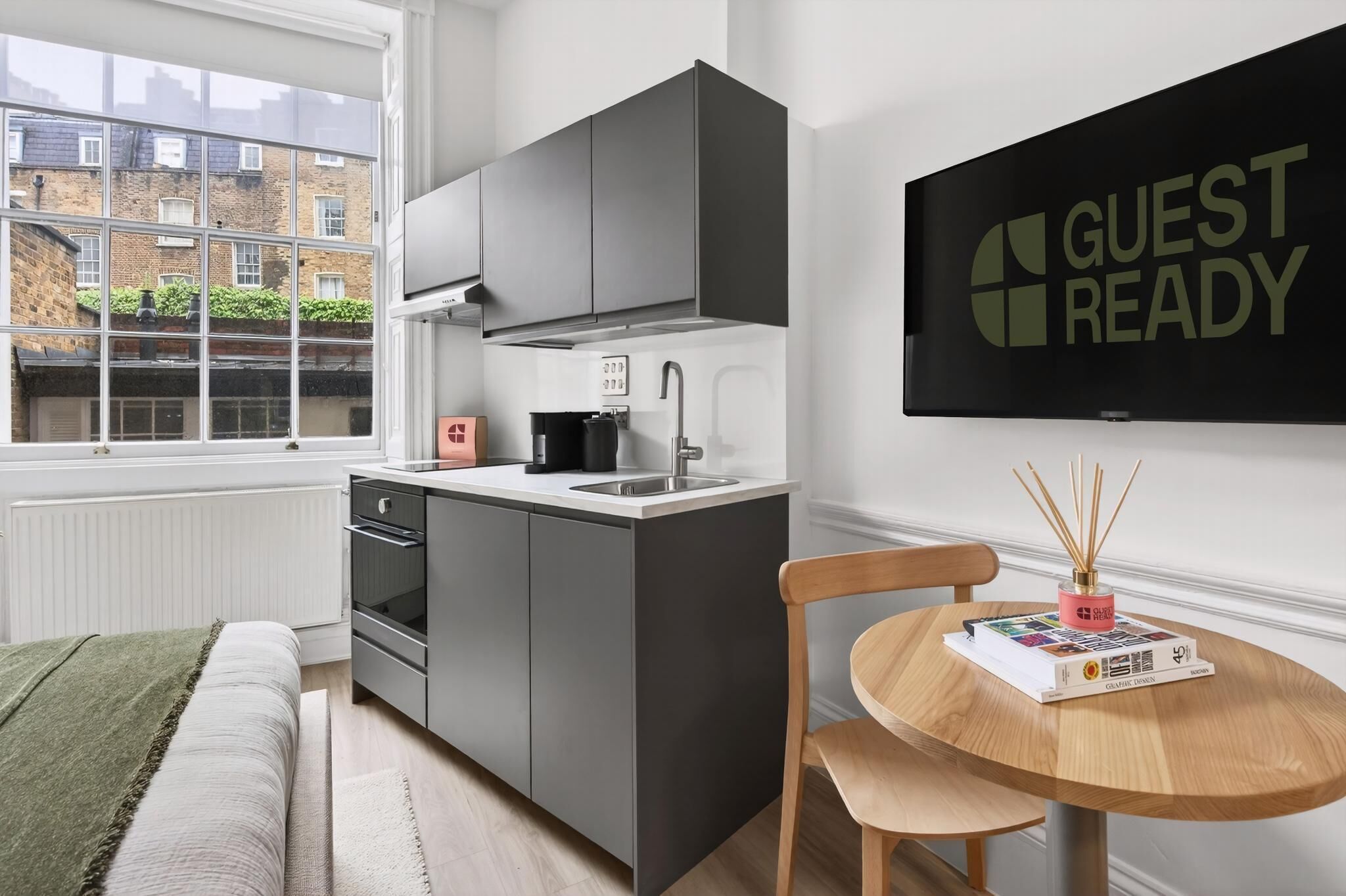 A modern kitchen with grey cabinets, a black kettle, and a 'GUEST READY' sign.