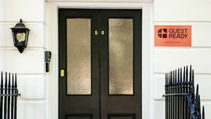 A black double door with a 'Guest Ready' sign, a black metal gate, and a white wall with a decorative arch above the door. - Guestready - The Crescent (London)