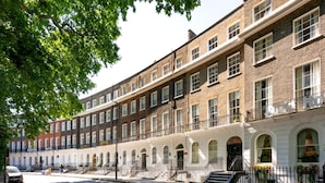 A row of traditional brick townhouses with arched windows and balconies, a white building with a sign 'Hotel,' and a clear street in front. - Guestready - The Crescent (London)