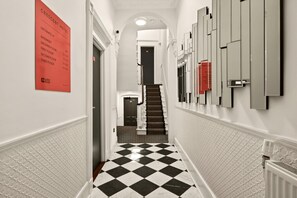 Un corridoio d'albergo con pavimento a scacchi, una scala e un cartello che indica l'ingresso alla cantina.