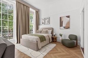 A bedroom with a large window, a bed, a chair, and artwork on the walls. - Guestready - The Crescent (London)