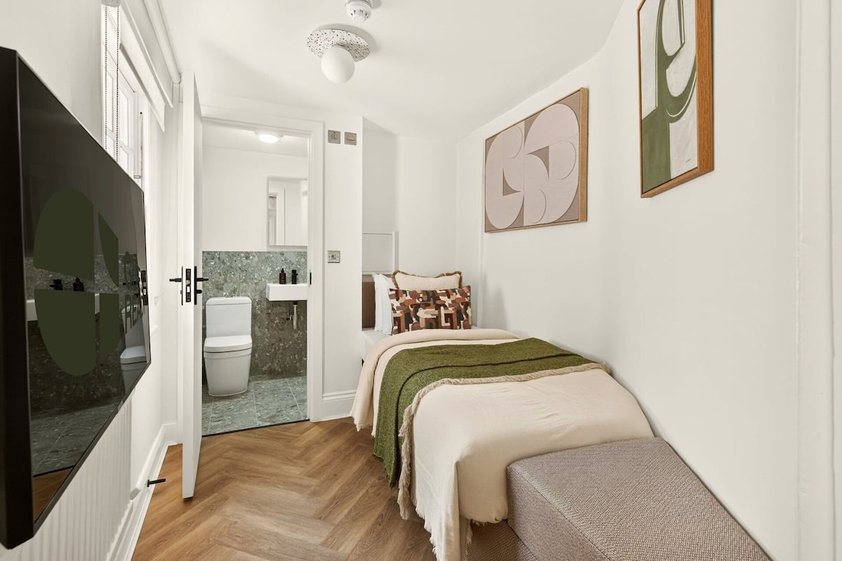 A bedroom with a bed, a bedside table, a mirror, and a window.