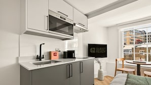 A modern kitchen with a built-in oven, a sink, and a coffee maker. There is a window with a city view and a framed sign on the wall. - Guestready - The Crescent (London)