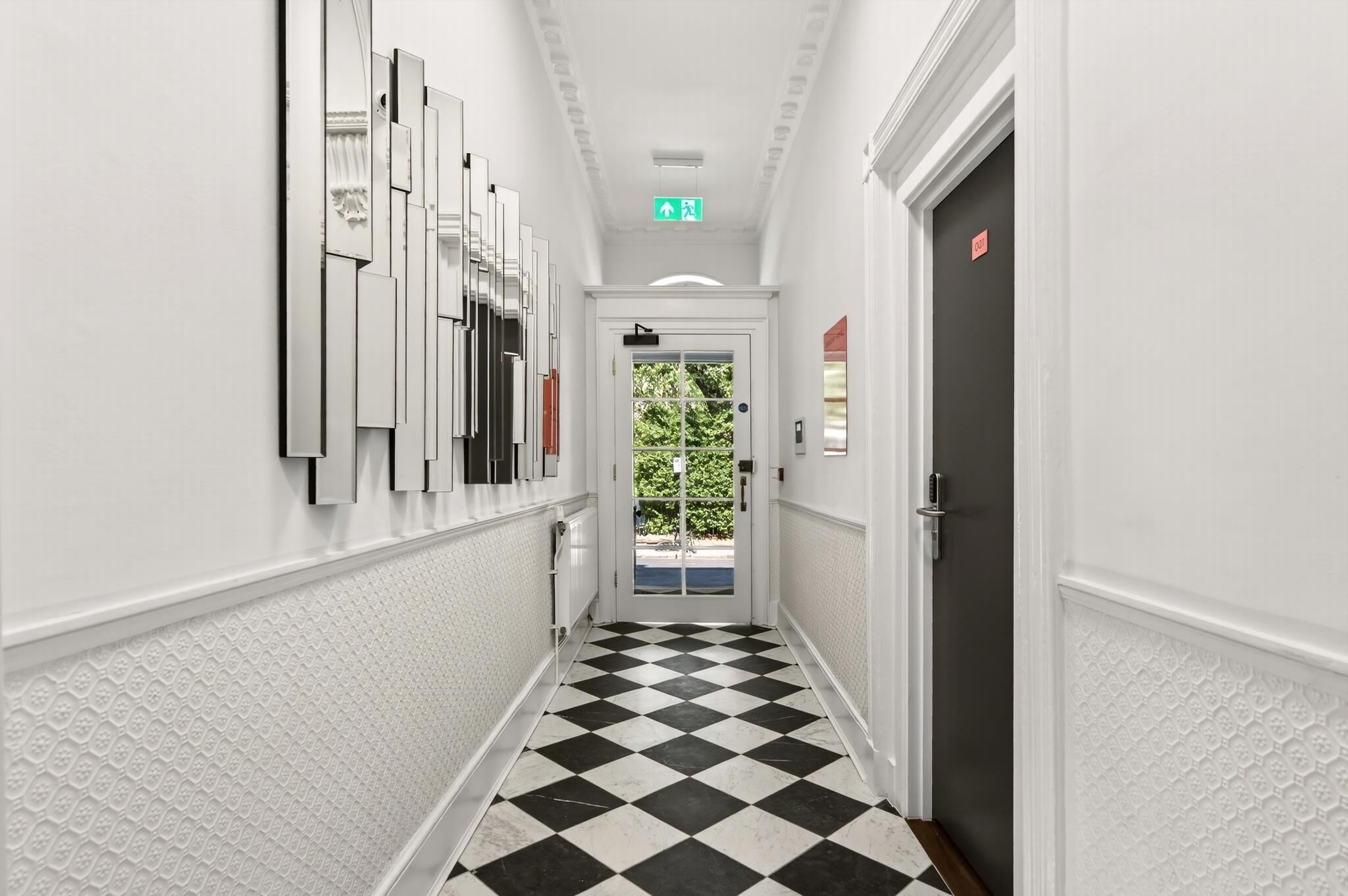 A hallway with a checkered floor, white walls, and a door with a red sign.
