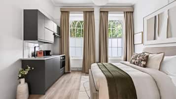 A modern bedroom with a large bed, a bedside table, and a built-in kitchen area with a coffee machine.