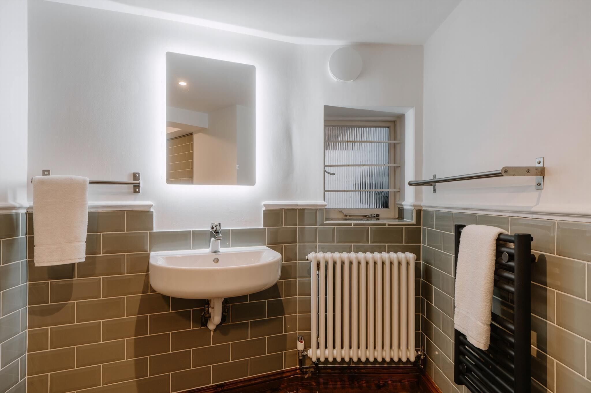 A bathroom with a sink, mirror, towel rack, radiator, and tiled walls.