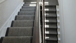 A stairway with a handrail, a window with a view of greenery, and a fire exit sign. - Guestready - The Crescent (London)