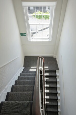 A stairway with a handrail, a window with a view of greenery, and a fire exit sign.