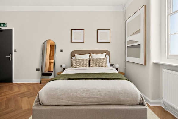 A bedroom with a bed, a mirror, a door, and framed artwork on the wall.