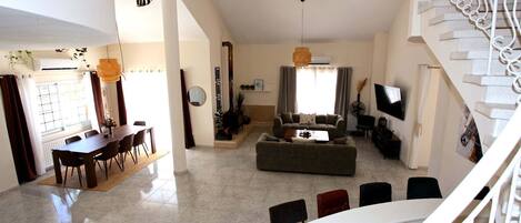 A spacious living area with a dining table, sofa, and a staircase.