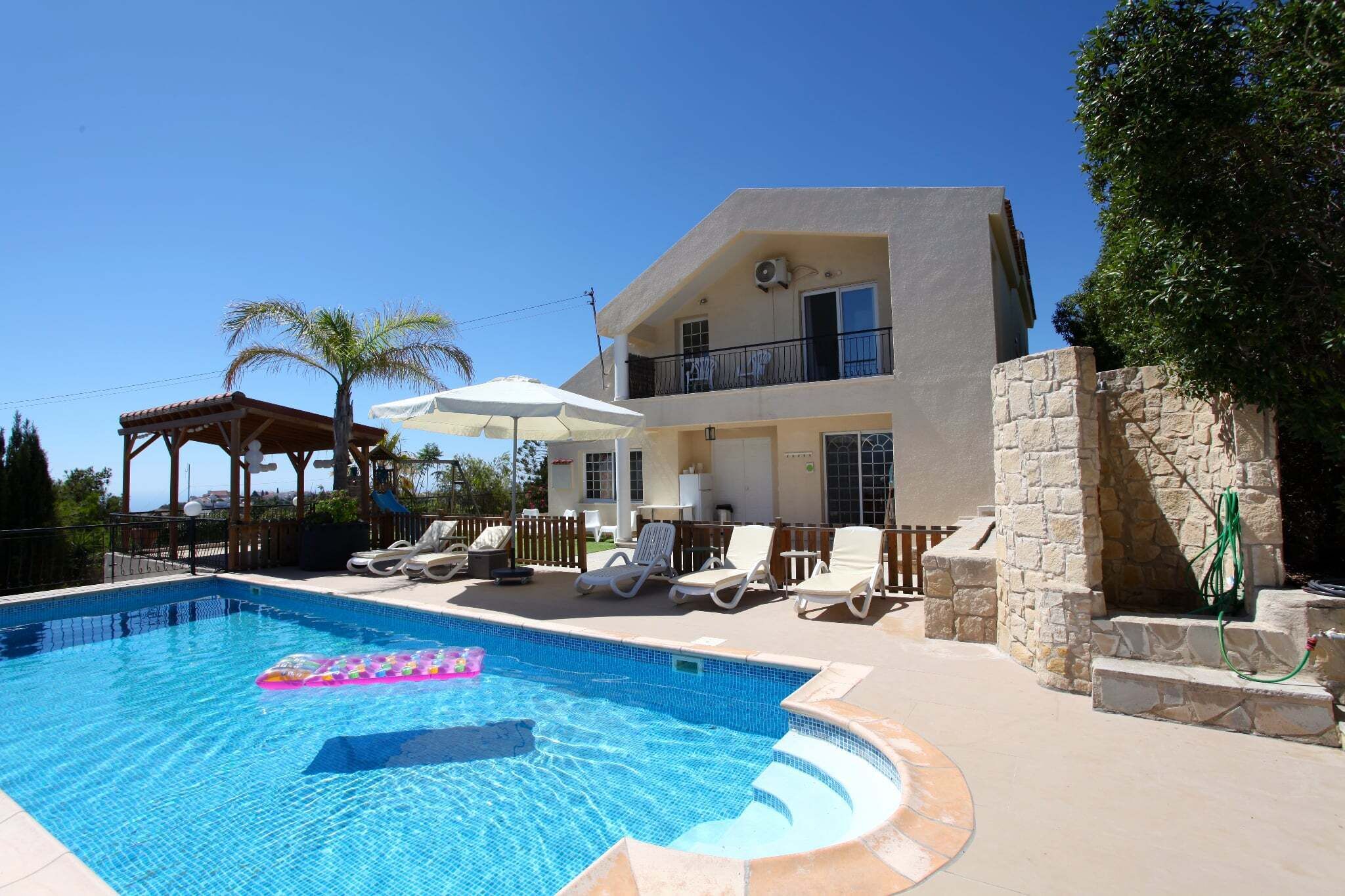 Ein zweistöckiges Gebäude mit Swimmingpool, Liegestühlen und einer Pergola.