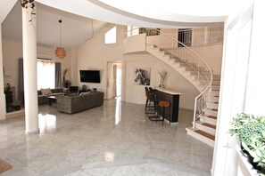 Een ruime woonkamer met een hoge plafond en een eethoek met barstoelen.