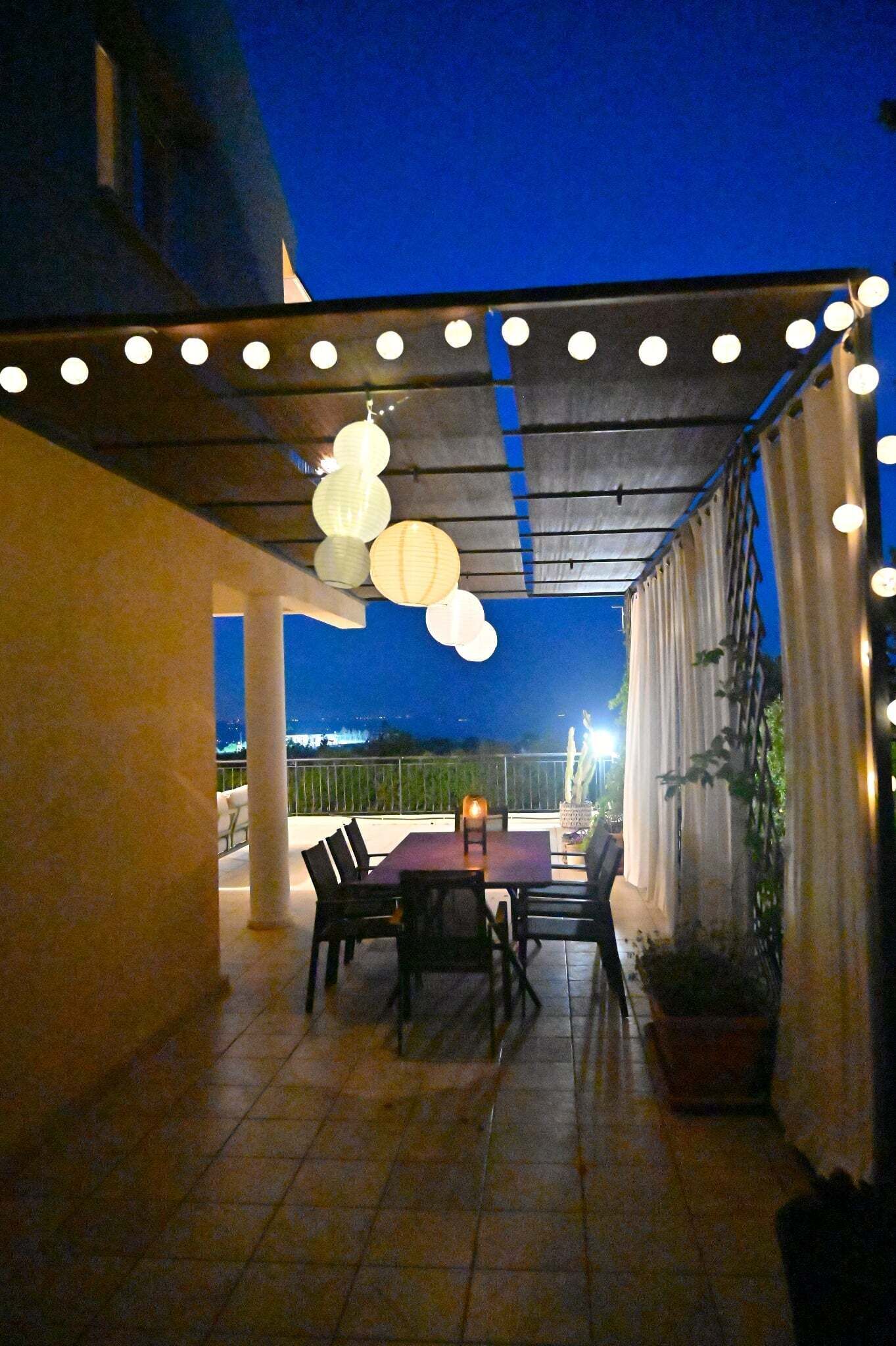An outdoor patio with a table and chairs, string lights, and potted plants.