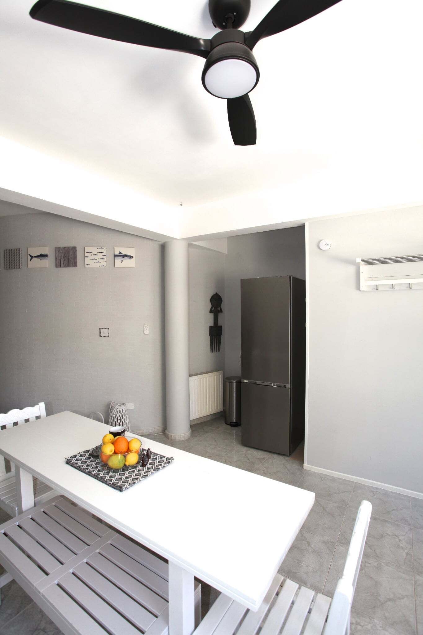 A modern kitchen with a white table, a fruit bowl, and a black refrigerator.