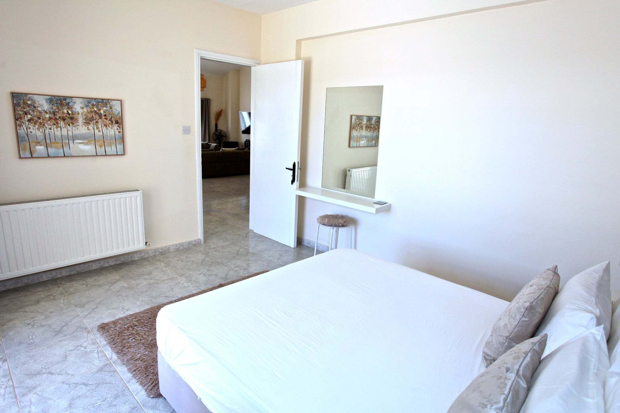 A bedroom with a bed, a radiator, a door leading to another room, and a mirror.