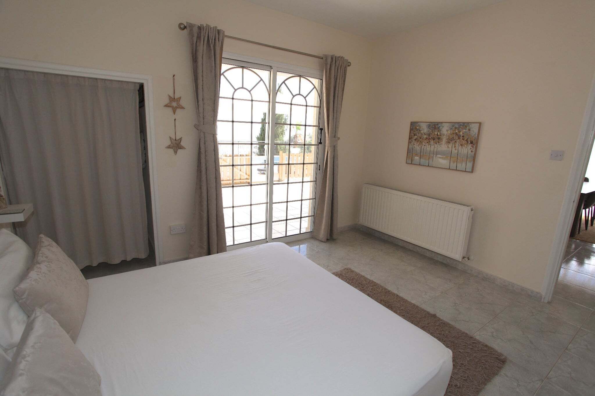 Un dormitorio con cama, radiador, ventana con cortinas y un cuadro en la pared.
