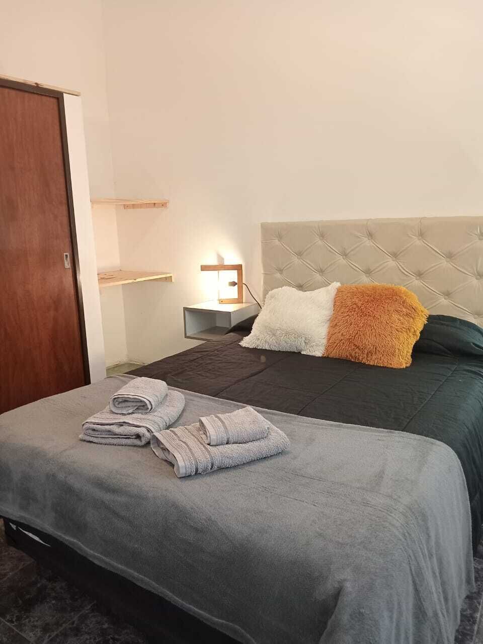 Una habitación de hotel con una cama, una mesita de noche, un estante en la pared y una puerta.