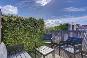 Eine Dachterrasse mit Holzdeck, zwei Bänken, einem Metallzaun und einem Hecken.