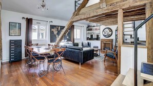 A spacious living area with a dining table, chairs, a sofa, and a staircase with exposed wooden beams. - Dartagnan S Vres Eclectic 2BR Home With Terrace (Paris)