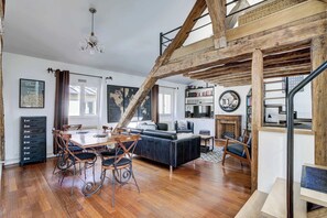 Ein geräumiger Wohnbereich mit Esstisch, Stühlen, einer Couch und einer Treppe mit freiliegenden Holzbalken.