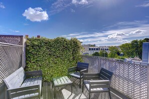 Ein Balkon mit Holzboden, einem Metallzaun und einer grünen Hecke.