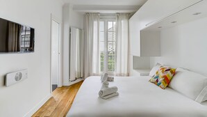 Ett modernt hotellrum med en stor säng, en platt-TV, ett element och ett fönster med gardiner.