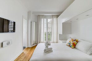 A modern hotel room with a large bed, a flat-screen TV, a radiator, and a window with curtains. - Charming Eiffel Stylish 1 BR With Parisian Charm (Paris)
