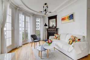 A living room with a white sofa, a black armchair, a round coffee table, and a fireplace. - Charming Eiffel Stylish 1 BR With Parisian Charm (Paris)
