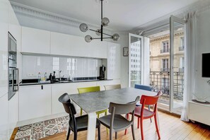 A modern kitchen with a dining area, large windows, and a view of the city. - Charming Eiffel Stylish 1 BR With Parisian Charm (Paris)
