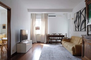 Ein Wohnzimmer mit Sofa, Fernseher, Esstisch, Stühlen und einem Schrank.
