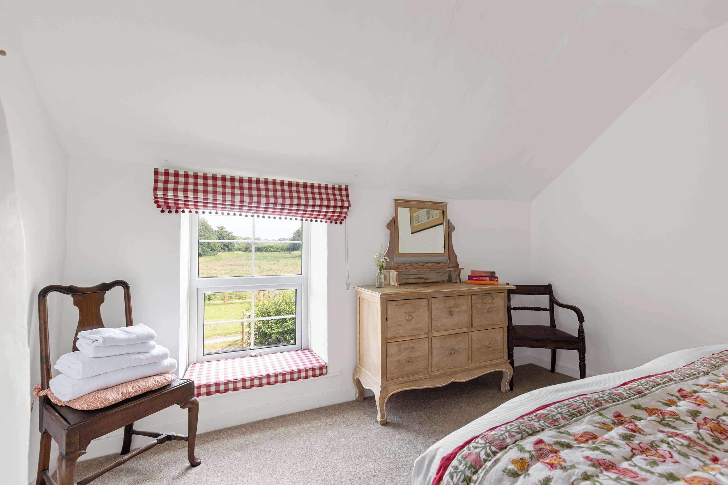 Une chambre avec une fenêtre, une commode en bois, une chaise et un lit.