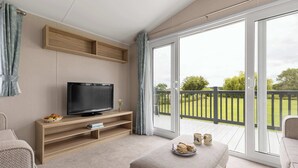 Ein modernes Wohnzimmer mit Flachbildfernseher, Holzregalen, einer Couch und einem Balkon mit Blick auf Grünflächen.