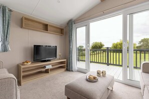 Ein modernes Wohnzimmer mit Flachbildfernseher, Holzregalen, einer Couch und einem Balkon mit Blick auf Grünflächen.