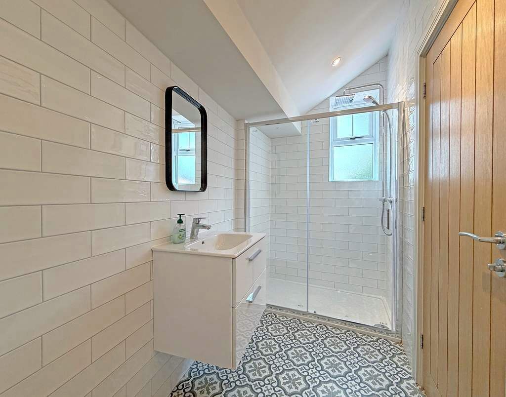 Un baño con paredes de azulejos blancos, un lavabo, un espejo, cabina de ducha y suelo estampado.