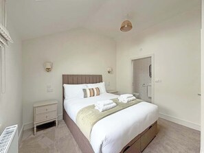 Een slaapkamer met een bed, nachtkastjes, een wandlamp, een deur en een radiator.