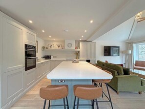 Een moderne keuken met een centraal eiland, barstoelen en een groene bank in een woonruimte.