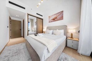 A modern hotel room with a large bed, bedside tables with lamps, a mirror, and a feather artwork on the wall. - Free Housekeeping Visits During Your Stay - Stayshort - 1 Bed Apartment in JVC That Sleeps 2 With Balcony (Dubai)