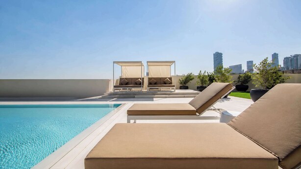 Un área de piscina en la azotea con sillones de descanso y un horizonte urbano al fondo.