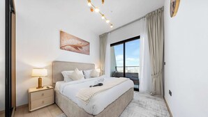 Un dormitorio moderno con una cama grande, una mesita de noche con lámpara, una ventana con cortinas y vistas a la ciudad.