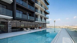 Un edificio moderno con piscina en la azotea, barandillas de vidrio y vistas despejadas del paisaje urbano.