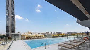 Una piscina en la azotea con tumbonas, cielo despejado y un paisaje urbano de fondo.
