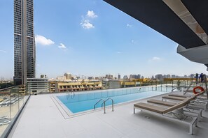 A rooftop pool with sun loungers, a clear sky, and a cityscape in the background. - Free Housekeeping Visits During Your Stay - Stayshort - 1 Bed Apartment in JVC That Sleeps 2 With Balcony (Dubai)