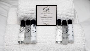 A white towel with a framed welcome card and five bottles of toiletries.