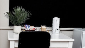 A white desk with a black chair, a potted plant, a coffee maker, and a trash can.