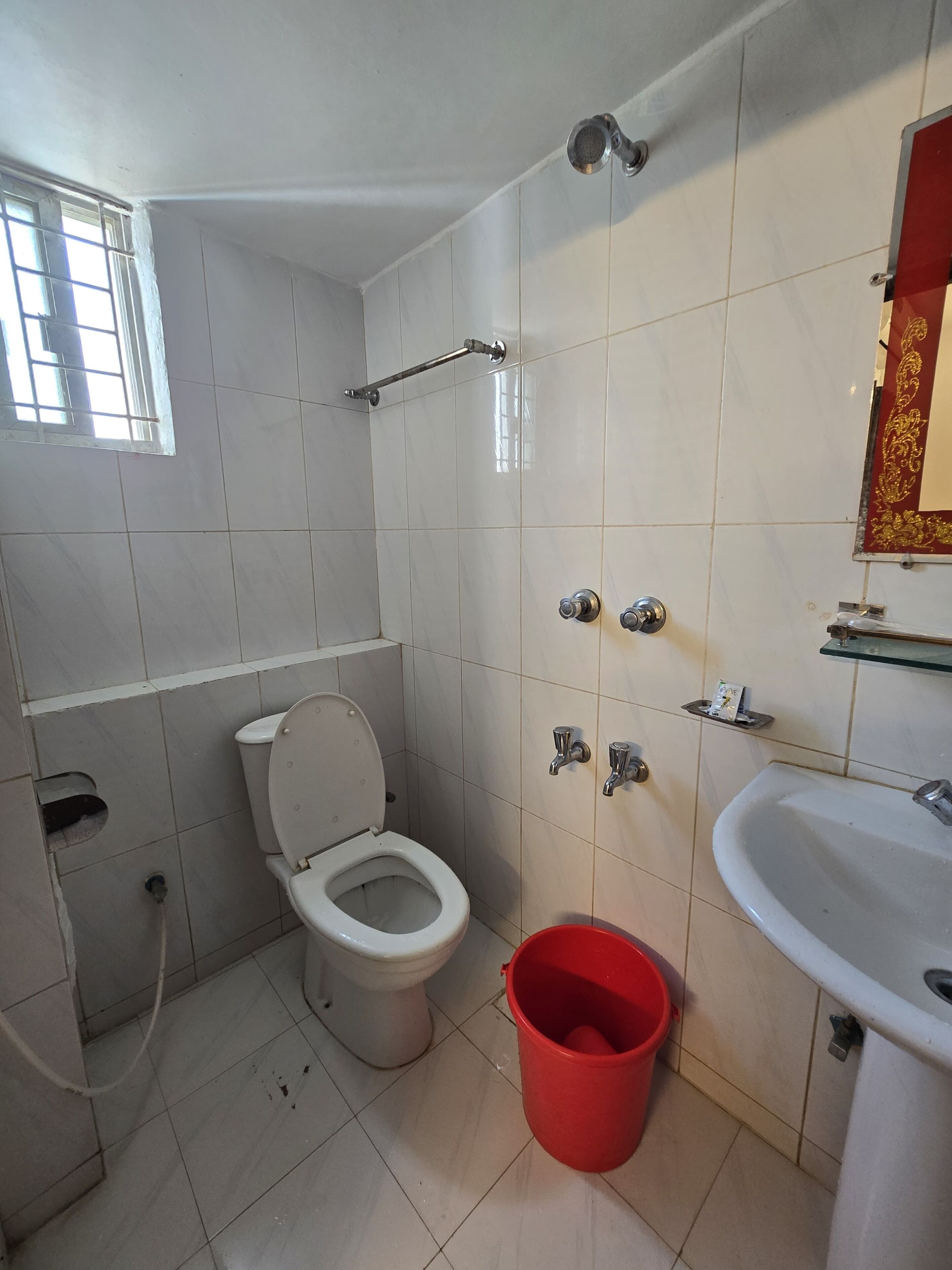 Un baño con inodoro, un cubo rojo, ducha y lavamanos.