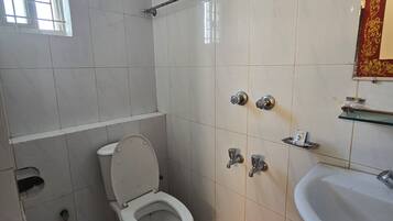 Un baño con inodoro, un cubo rojo, ducha y lavamanos.