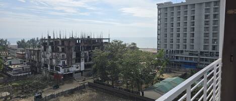 A view from a balcony overlooking a construction site with a building under construction, a beach, and a high-rise building in the background.