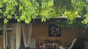 Un área de estar exterior con mobiliario de mimbre, una mesa de comedor y un cuadro colgado en la pared.